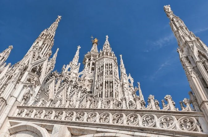 Carved marble spires of Milan Cathedral against a deep blue sky
